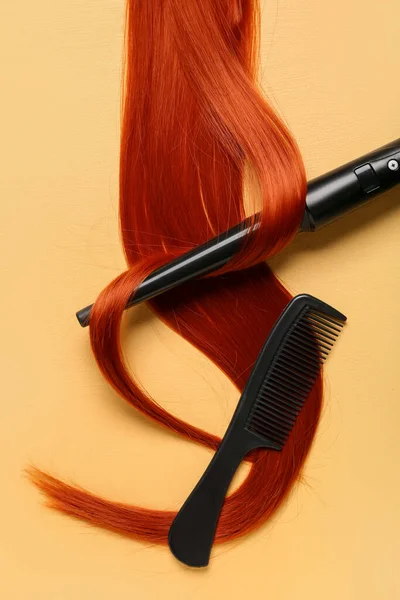 Ginger hair strand, comb and curling iron on yellow background, closeup