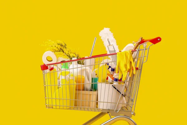 黄色の背景に花と掃除用品でいっぱいのショッピングカート — ストック写真