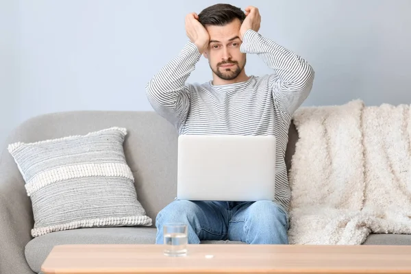 stock image Young man with laptop suffering from headache at home