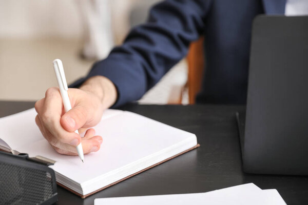 Young businessman working with notebook at table in office, closeup