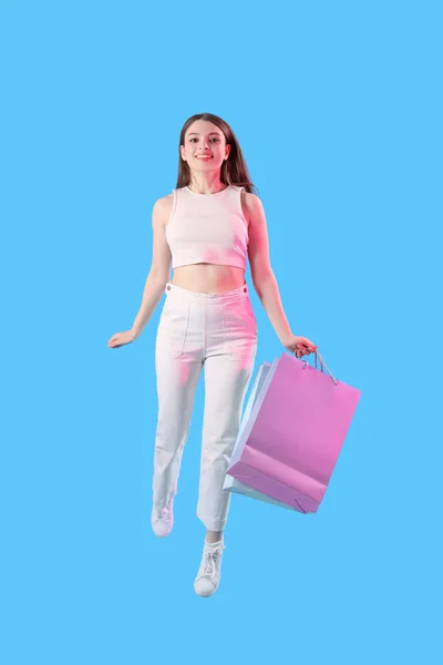 Alışveriş Çantalı Genç Bir Kadın Mavi Arka Planda Zıplıyor — Stok fotoğraf