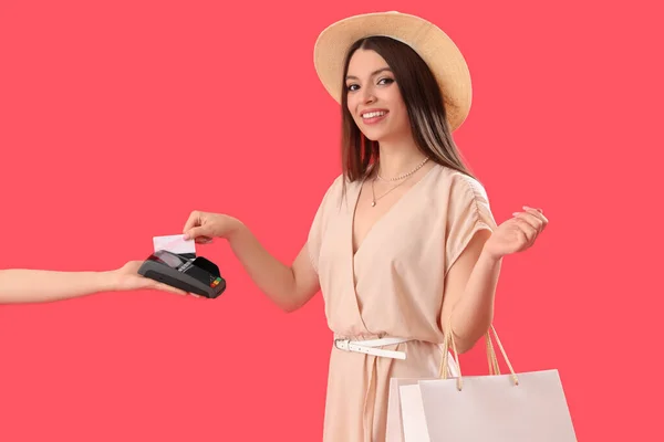 Alışveriş Çantalı Genç Bir Kadın Kırmızı Arka Planda Terminalden Ödeme — Stok fotoğraf