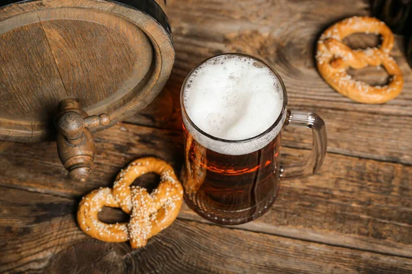 stock image Mug of cold beer, pretzel and barrel on wooden background. Oktoberfest celebration