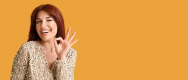 Güzel kızıl saçlı kadın turuncu arka planda mesaj için yeri olan iyi niyet gösterisi yapıyor.