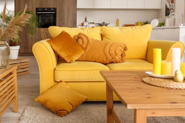 Açık uzay mutfağının içinde sarı kanepe ve ahşap sehpa var.