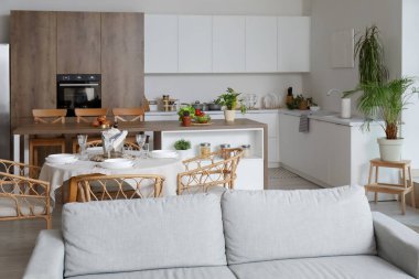 Açık uzay mutfağının içinde gri kanepe, yemek masası ve ada servis edilir.