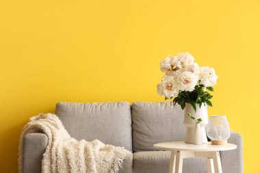 Kahve masalı beyaz şakayıklar ve sarı duvarın yanındaki kanepe.