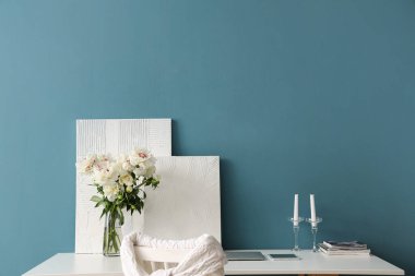 Mavi duvarın yanındaki masada beyaz şakayık ve tablo vazosu.