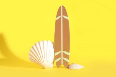 Sarı arka planda deniz kabukları olan mini sörf tahtası.