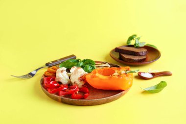 Izgara sebzeli tabak ve sarı arka planda fesleğen.