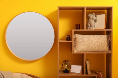 Oturma odasındaki sarı duvarda asılı yuvarlak ayna.