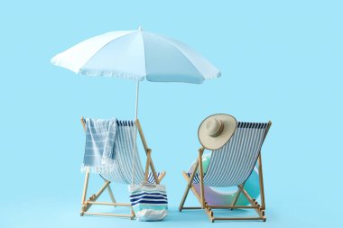 Mavi arka planda şezlonglar, şemsiyeler ve plaj aksesuarları olan yaz kompozisyonu. Yaz tatili kavramı