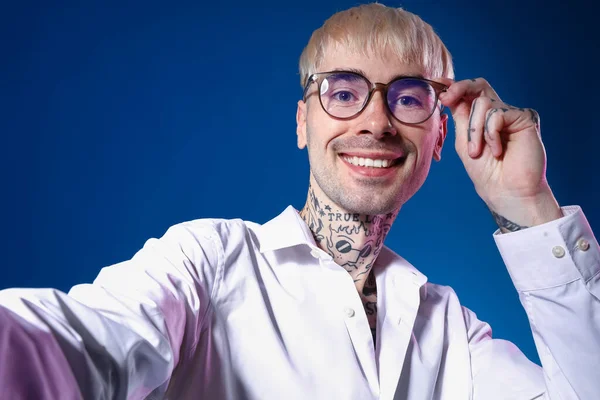 Ung Tatuerad Man Glasögon Tar Selfie Blå Bakgrund Närbild — Stockfoto