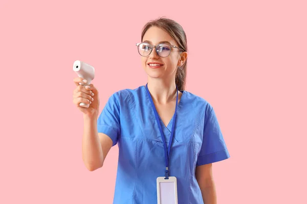 ピンクの背景に赤外線温度計を持つ女性医療インターン — ストック写真