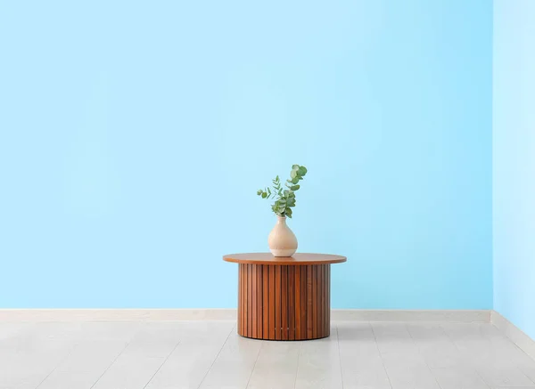 青い壁の近くの花瓶にユーカリの枝を持つ木製のコーヒーテーブル — ストック写真