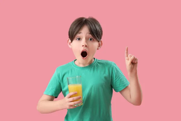 Zszokowany Chłopczyk Szklanką Soku Pomarańczowego Wskazującą Coś Różowym Tle — Zdjęcie stockowe