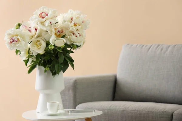 ソファの近くのテーブルの上にコーヒーと携帯電話のカップと白い牡丹の花瓶 — ストック写真
