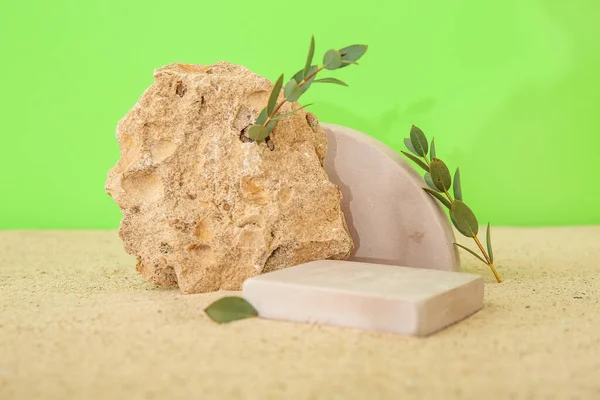 stock image Decorative plaster podiums with tree branches and stone on sand against green background