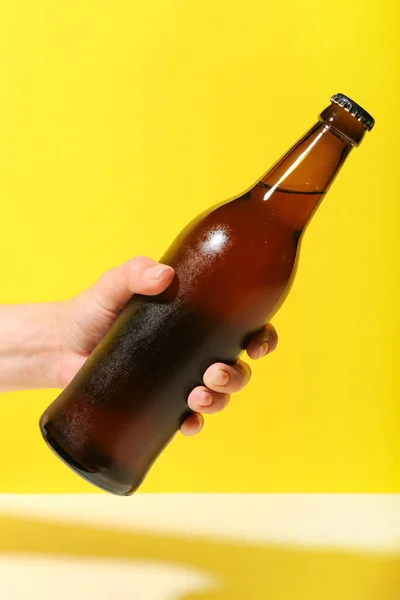 stock image Female hand with bottle of cold beer on yellow background