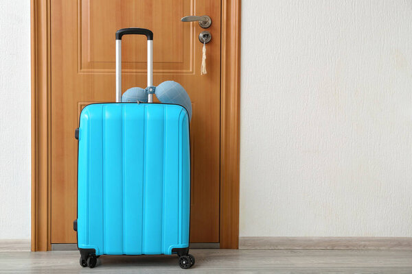 Blue suitcase with travel cushion near door in room. Travel concept