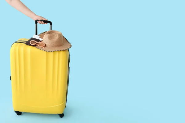 stock image Female hand with suitcase, wicker hat and sunglasses on blue background. Travel concept