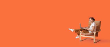 Dizüstü bilgisayarlı, turuncu arka planda koltukta oturan, mesaj için yeri olan güzel genç bir kadın.