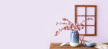 Çiçek açan ağaç dalları, cam, tabak ve peçeteyle aydınlık duvarın yanındaki ahşap masada. Tasarım için pankart