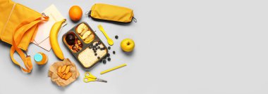 Gri arka planda lezzetli yemek ve okul malzemeleriyle dolu beslenme çantası ve mesaj için yer.