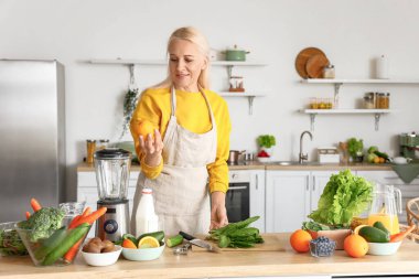 Taze sebzeli ve meyveli olgun bir kadın mutfakta sağlıklı meyve suyu yapıyor.