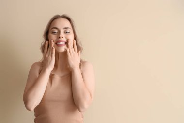 Bej arka plan üzerinde yüz geliştirme egzersizi yapan genç bir kadın.