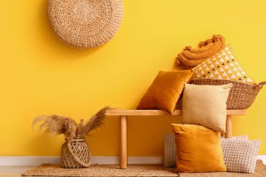 Sarı duvarın yanındaki bankta şık yastıklı sepet.