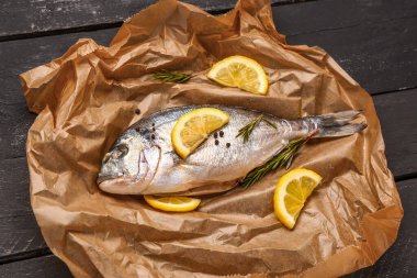 Koyu ahşap arka planda limonlu çiğ dorado balığı.