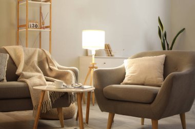 Oturma odasının içinde rahat gri kanepe, koltuk ve parlak lamba.
