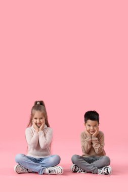 Pembe arka planda oturan süveter giymiş şirin çocuklar.