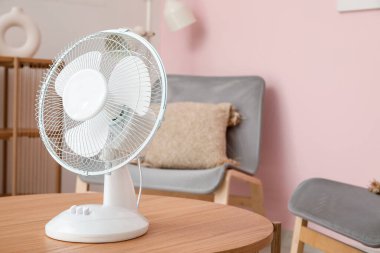 Oturma odasının içinde modern elektrikli vantilatör olan masa.