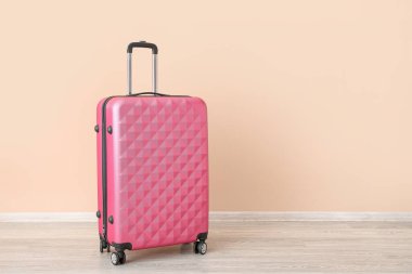 Soluk turuncu duvarın yanında pembe bavul. Seyahat kavramı
