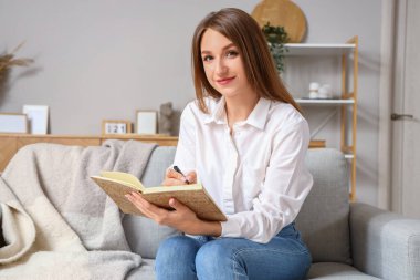 Not defteri olan genç bir kadın evdeki kanepede sohbet ediyor.