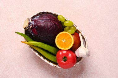 Pembe arka planda farklı taze meyve ve sebzelerle dolu bir hasır kase.