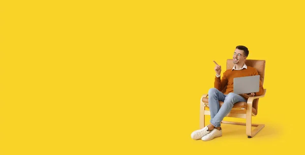 stock image Young man with laptop sitting in armchair on yellow background with space for text