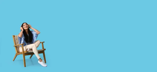 Красивая Молодая Женщина Наушниками Сидящая Деревянном Кресле Светло Голубом Фоне — стоковое фото