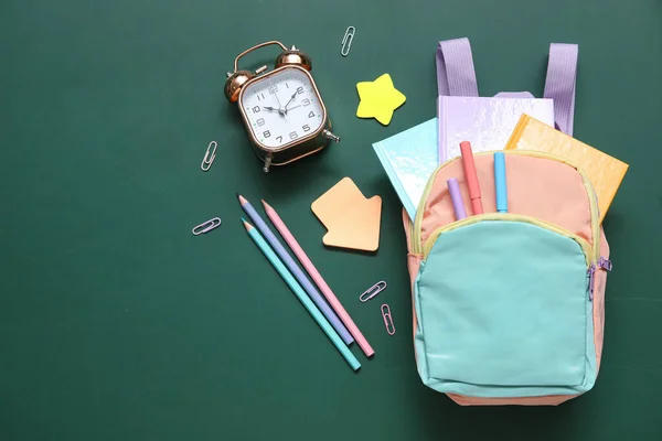 緑の背景に目覚まし時計 ノートや鉛筆とカラフルな学校のバックパック — ストック写真