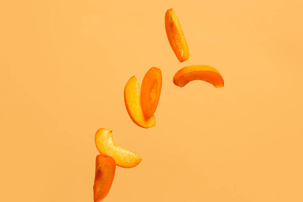 Flying pieces of fresh apricot on orange background
