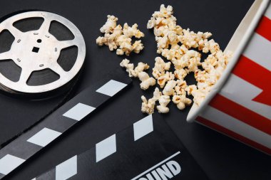 Lezzetli patlamış mısır, alkış tahtası ve siyah arka planda film makarası.