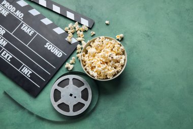 Lezzetli patlamış mısırlı kase, alkış tahtası ve yeşil arka planda film makarası.