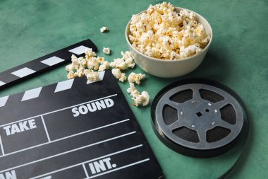 Lezzetli patlamış mısırlı kase, alkış tahtası ve yeşil arka planda film makarası.