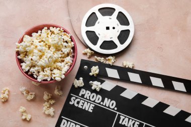 Lezzetli patlamış mısır, alkış tahtası ve arka planda film makarası olan bir kase.