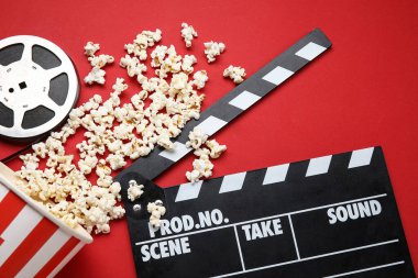 Lezzetli patlamış mısır, el çırpma tahtası ve kırmızı arka planda film makarası.