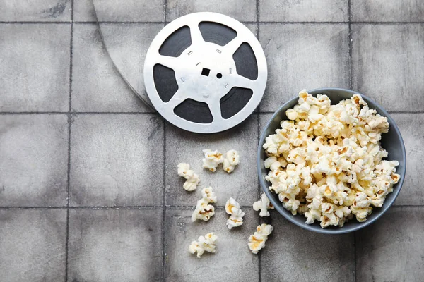 Schüssel Mit Leckerem Popcorn Und Filmrolle Auf Grauem Fliesenhintergrund — Stockfoto