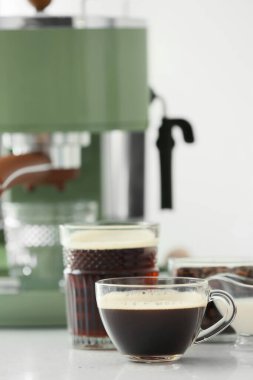 Mutfaktaki masada bir fincan sıcak espresso ve modern kahve makinesi.