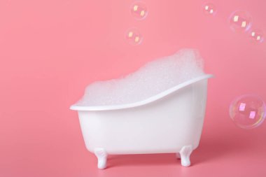 Köpüklü küçük küvet ve pembe arka planda sabun köpükleri.